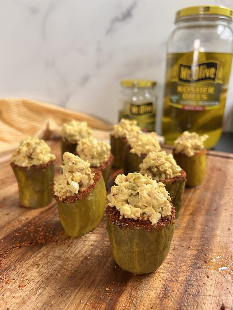 Chicken Salad Stuffed Pickles arranged on a wooden cutting board with a jar of Mt. Olive Kosher Dills in the background