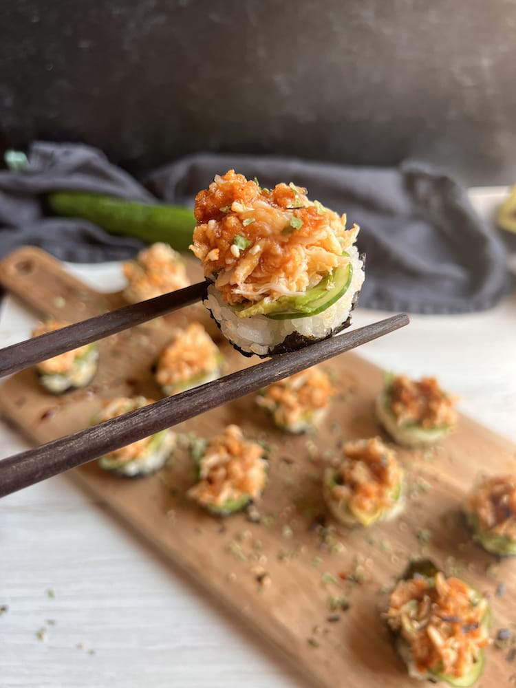 Spicy Crab Sushi Cups on a cutting board with one sushi bite held by chopsticks toward the camera