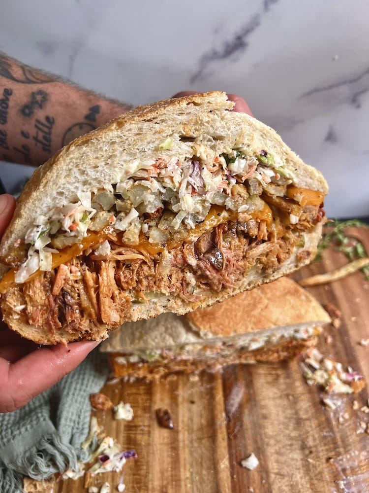 Pittsburgh Style Smoked Pork Sandwich held by two hands over a wooden cutting board