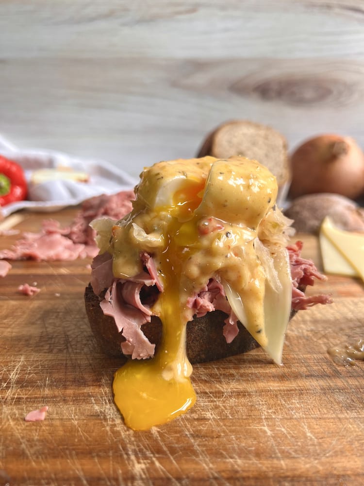 Reuben Benedict with poached egg sliced open and yolk dripping down on wooden cutting board