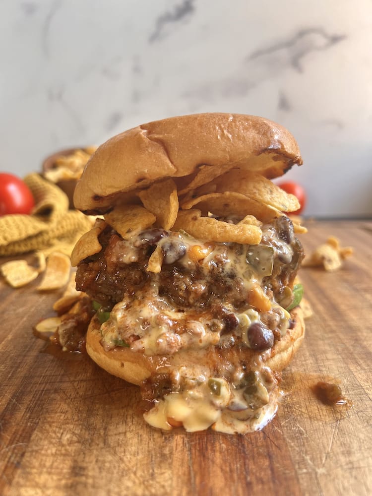 A Corn Chip Chili Cheese Burger on a wooden cutting board