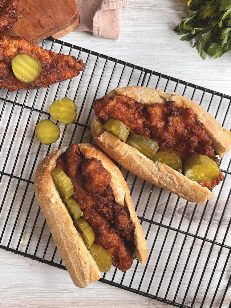 Two Nashville Hot Catfish Sandwich sitting on a black wire baking rack with dill pickle slices next to them