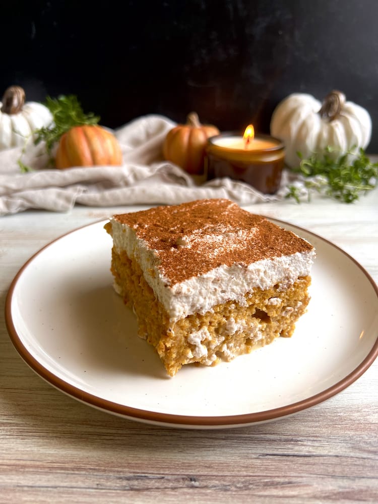 A slice of Pumpkin Tres Leches on a plate with pumpkin decorations in the background