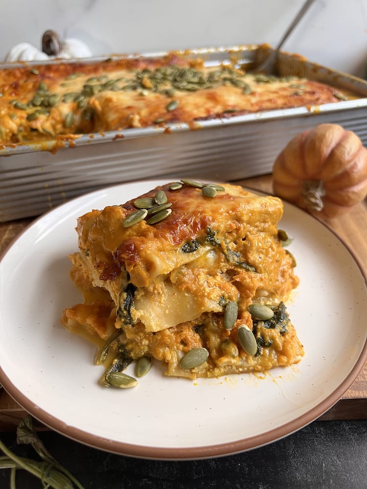 A serving of Pumpkin Lasagna on a white plate with the remaining pan of lasagna behind it