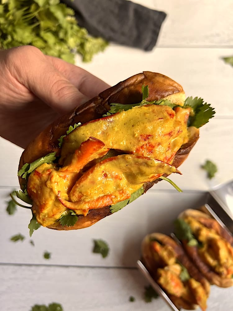 Curry Lobster Roll held in a hand with two more Lobster Rolls below