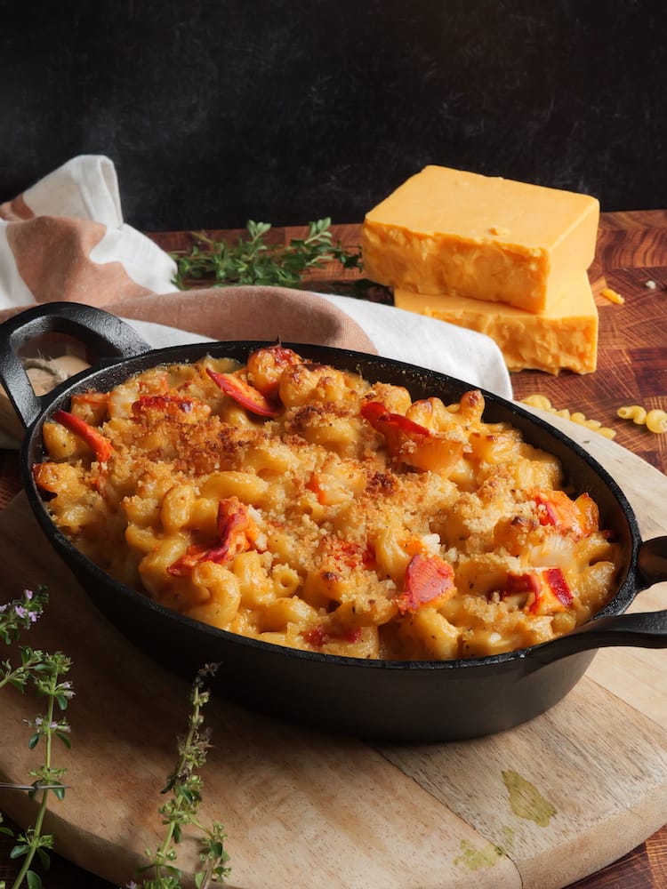 Lobster Mac and Cheese in a cast iron baking dish with blocks of cheese in the background