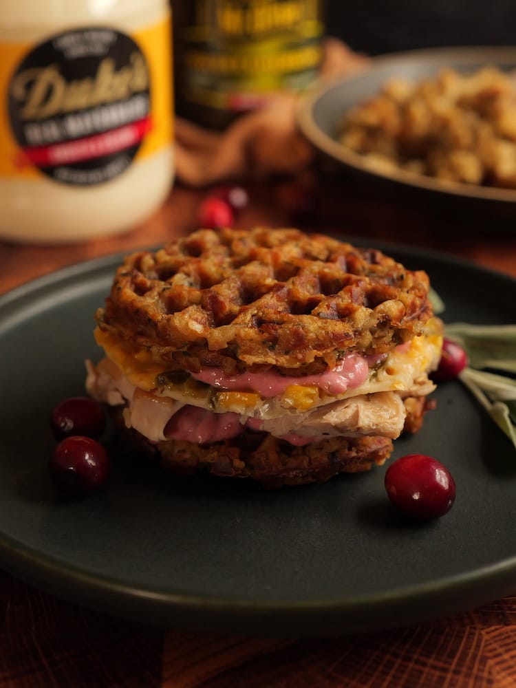 A Thanksgiving Leftovers Sandwich on a black plate with leftovers and jars of mayonnaise and pickles in the background