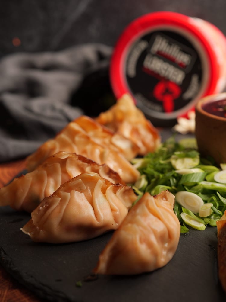 Lobster Potstickers on a black slate with fresh scallion slices around them and a can of Phillips Lobster in the background