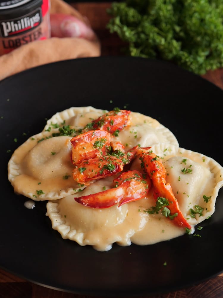 Lobster Ravioli on a black plate with fresh herbs and a jar of lobster in the background