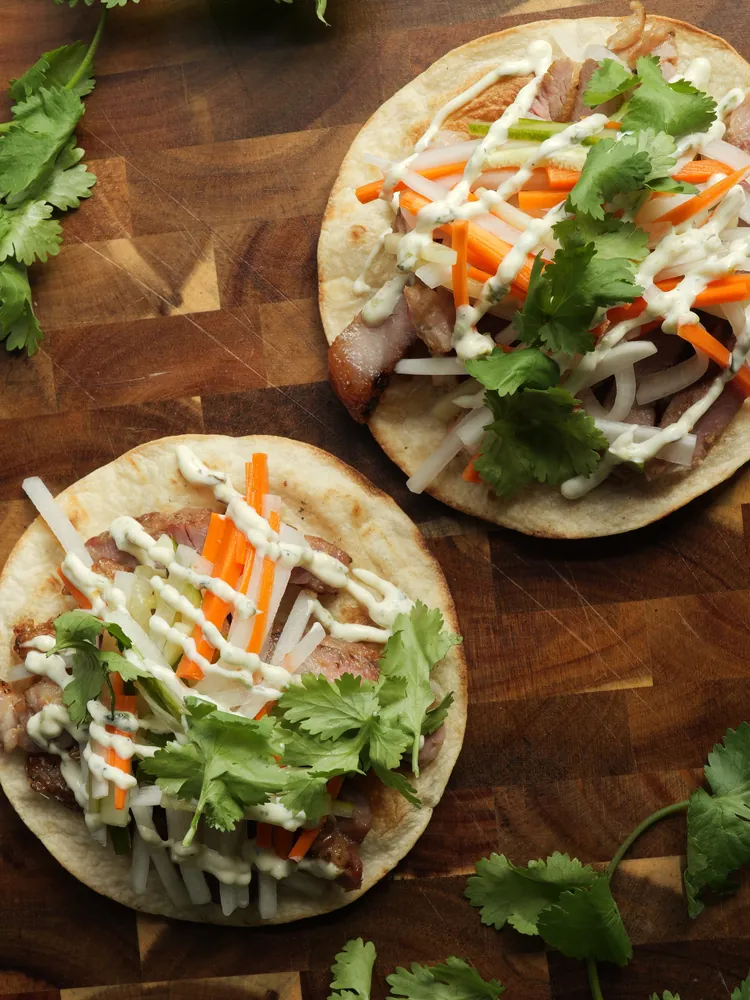 Two Banh Mi Tostada on a wooden cutting board (overhead shot)