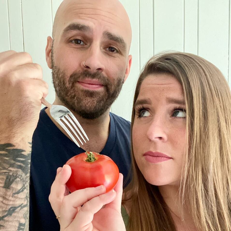 The two members of Hangry in Love. Zach holding a fork over a tomato that Sarah is holding