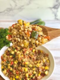 Squash & Red Pepper Couscous on a wooden spoon above a serving dish